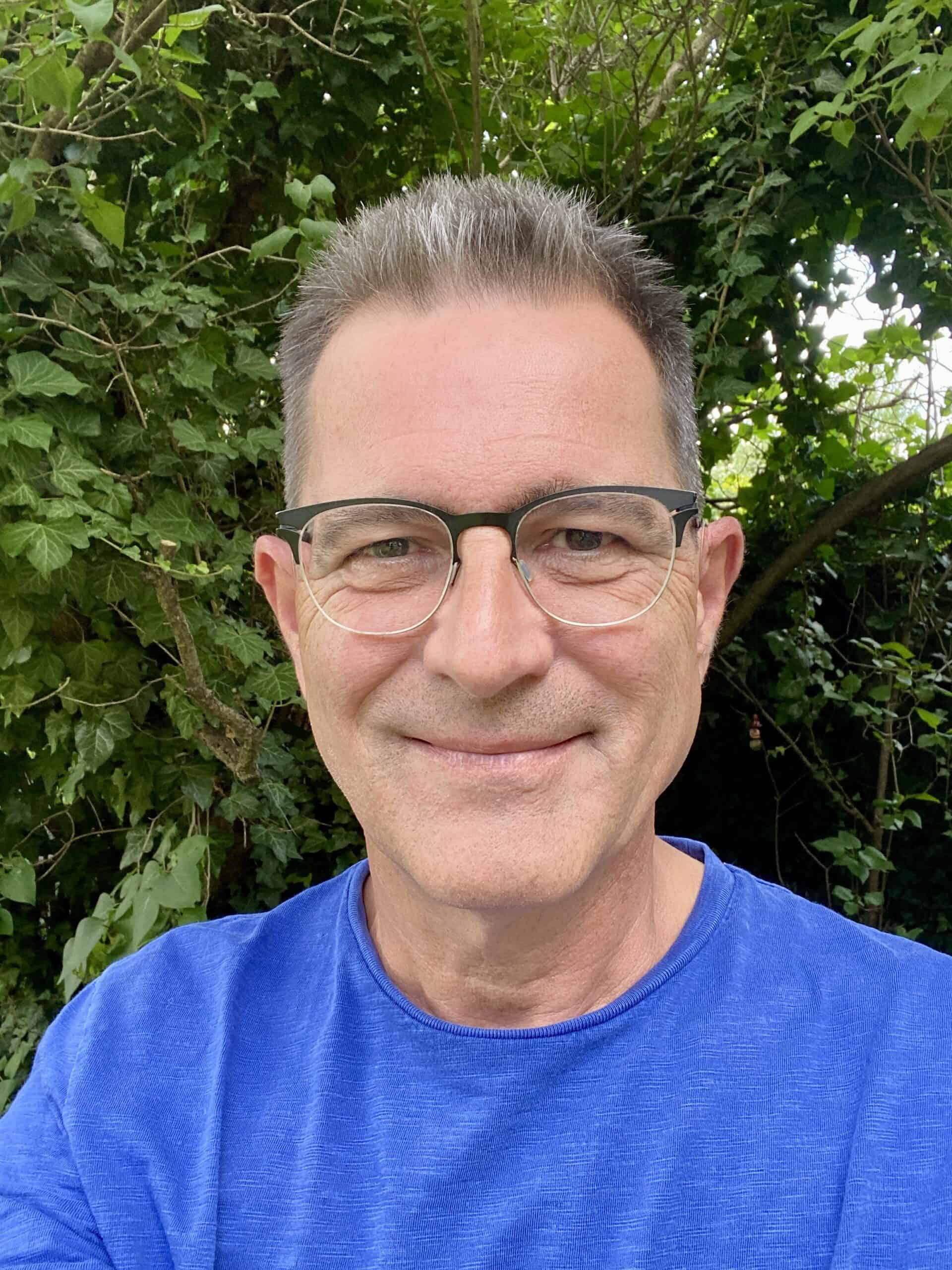 Portrait eines Mannes mit Brille vor grünem Laub, Symbol für Menschlichkeit in der KI-Ära.